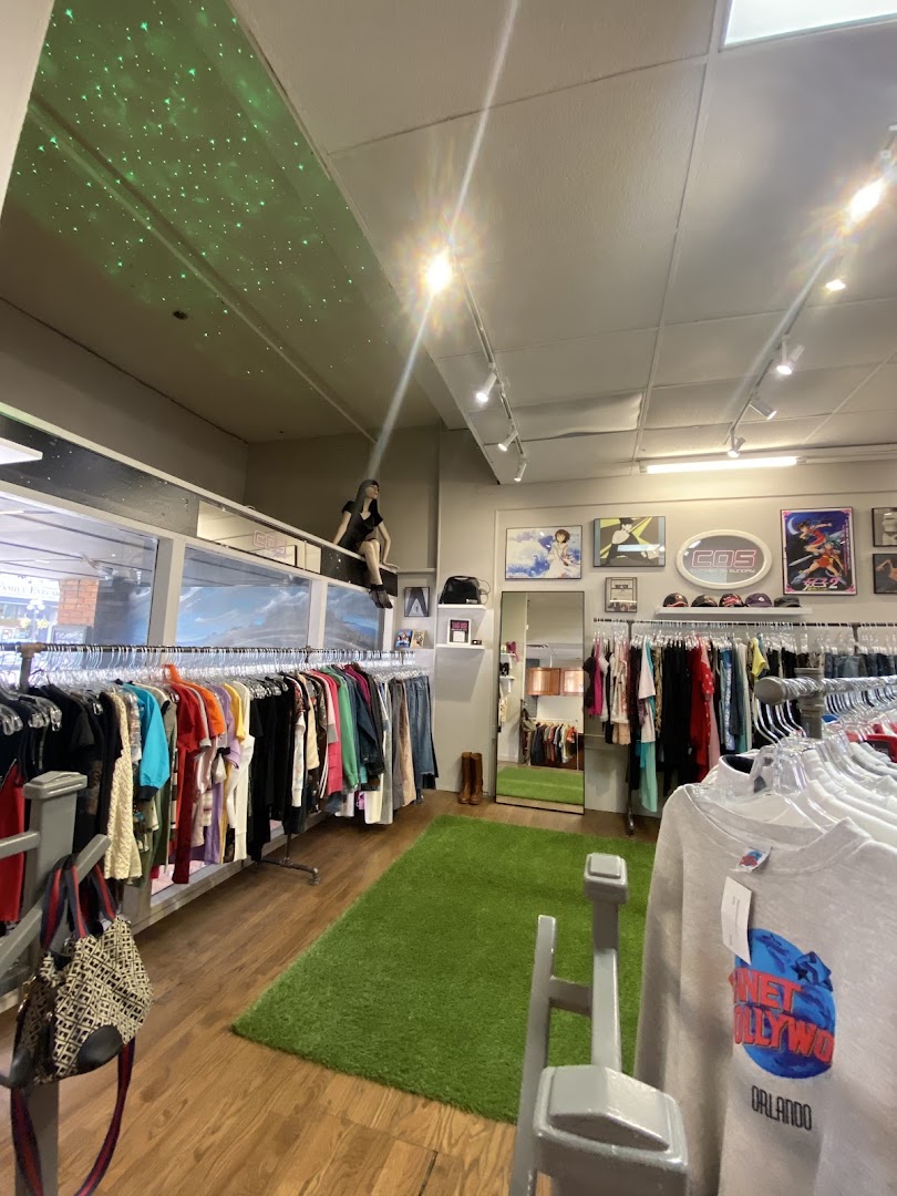 A shop corner with a star-patterned ceiling, green astroturf rug, anime posters on the wall, and a mannequin seated above a rack of colorful clothing.