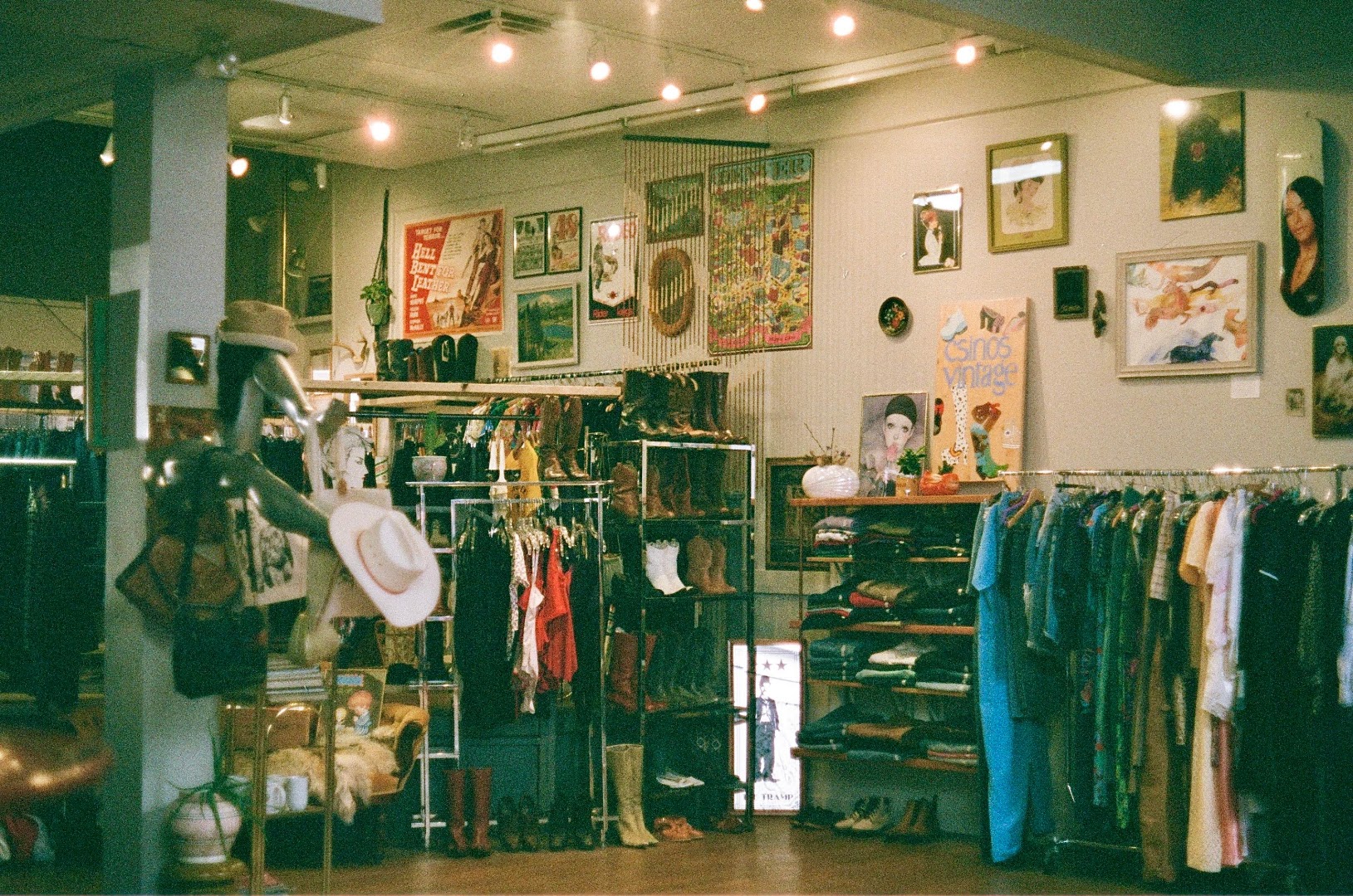 A cozy corner of the shop with a 'Star Vintage' sign, boots on open shelving, a small round table with fresh flowers, and a vintage 'Hell Bent for Leather' poster on the wall.